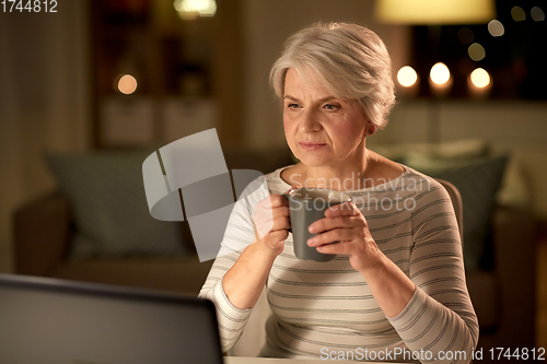 Image of senior woman with laptop drinking coffee at home