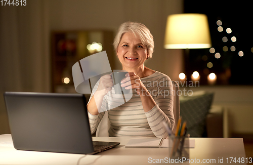 Image of senior woman with laptop drinking coffee at home