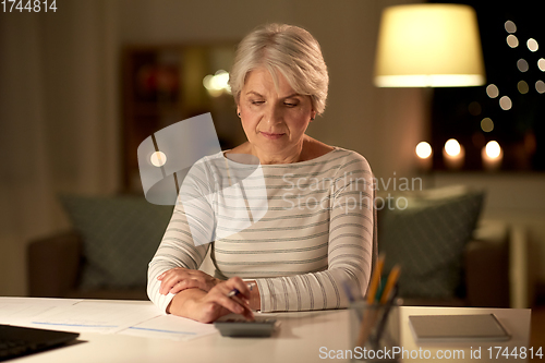 Image of old woman counting on calculator at home at night