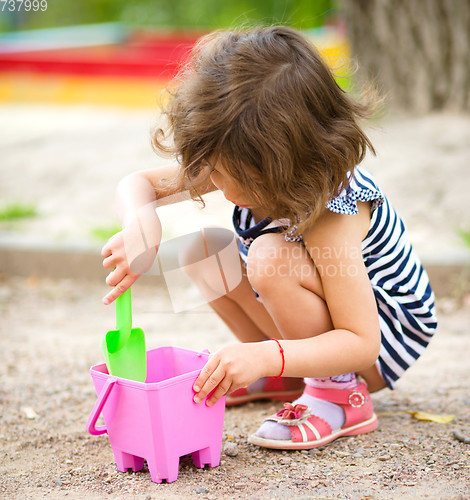 Image of Little girl is playing with sand in playground