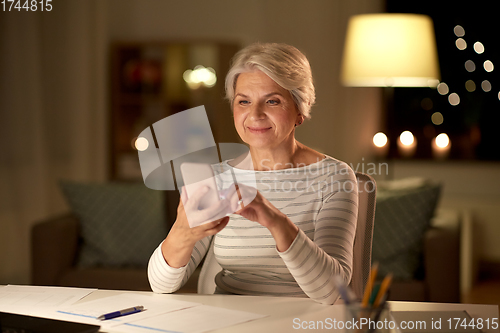 Image of senior woman with smartphone at home at night