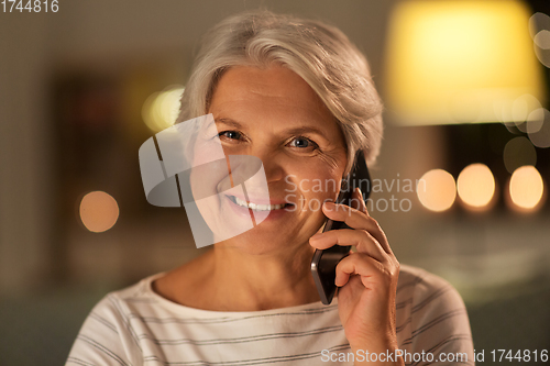 Image of old woman calling on smartphone at home in evening