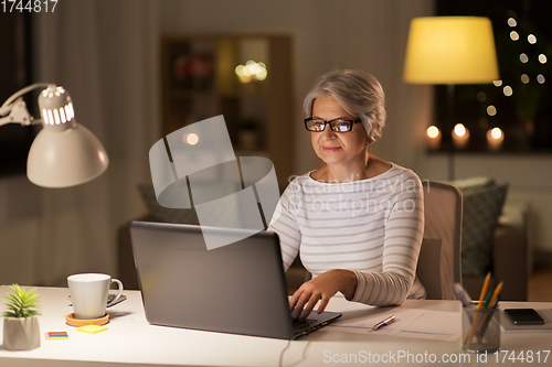 Image of senior woman with laptop working at home at night