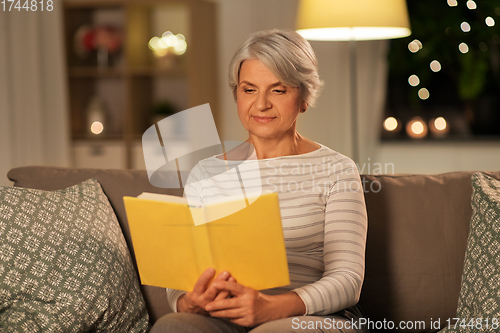 Image of happy senior woman reading book at home in evening