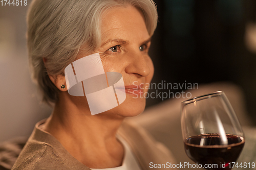 Image of senior woman drinking red wine at home in evening