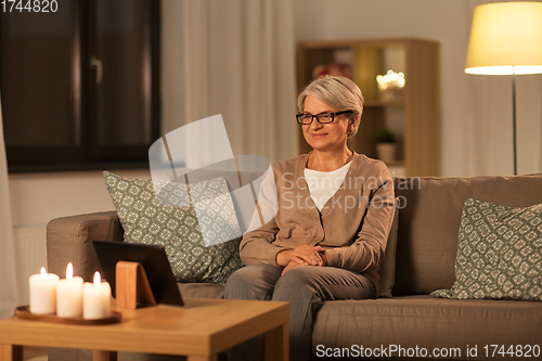 Image of happy senior woman with tablet pc at home at night