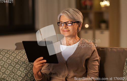 Image of happy senior woman with tablet pc at home at night