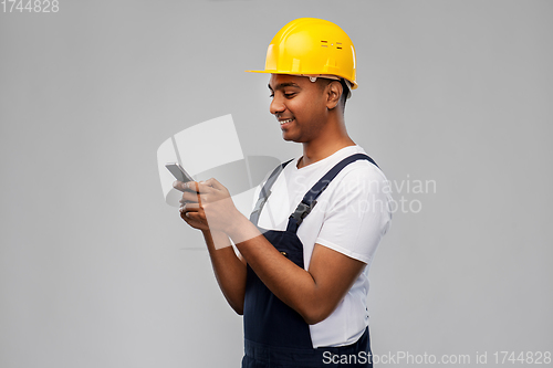 Image of happy indian or builder in helmet using smartphone