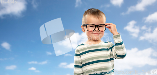 Image of portrait of smiling boy in glasses over blue sky