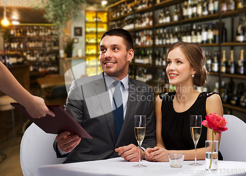 Image of waiter giving menu to happy couple at restaurant