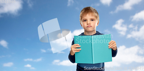 Image of displeased little boy with book over blue sky