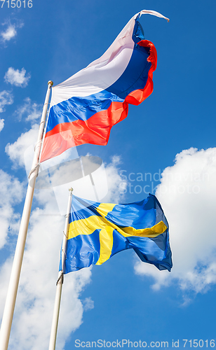 Image of Russian and Sweden flags waving against the blue sky