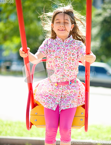 Image of Young happy girl is swinging in playground