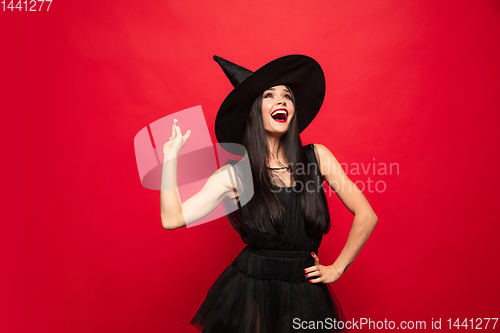 Image of Young woman in hat and dress as a witch on red background