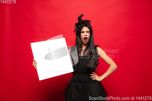 Image of Young woman in hat and dress as a witch on red background