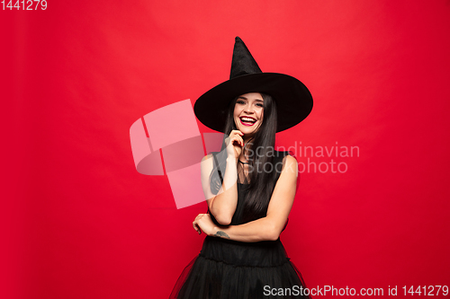 Image of Young woman in hat and dress as a witch on red background