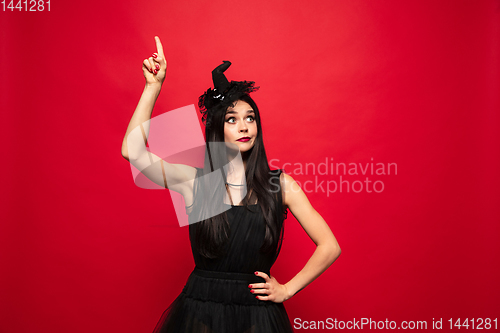 Image of Young woman in hat and dress as a witch on red background