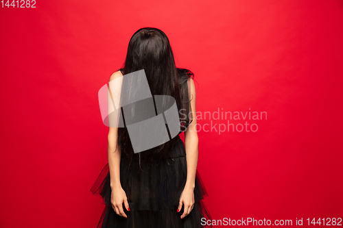 Image of Young woman in hat and dress as a witch on red background