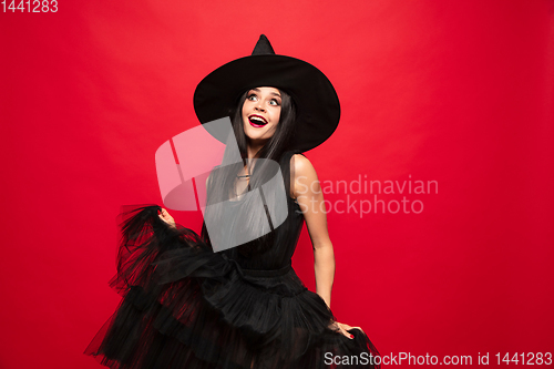 Image of Young woman in hat and dress as a witch on red background