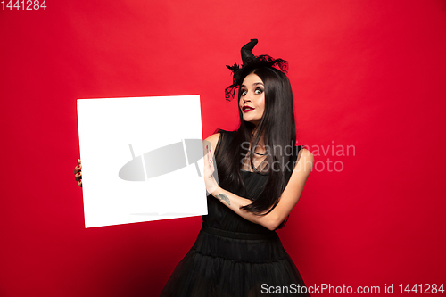 Image of Young woman in hat and dress as a witch on red background