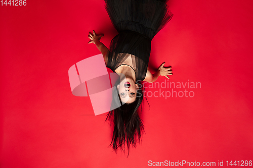 Image of Young woman in hat and dress as a witch on red background