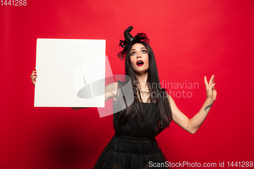 Image of Young woman in hat and dress as a witch on red background