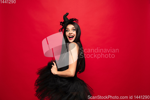 Image of Young woman in hat and dress as a witch on red background
