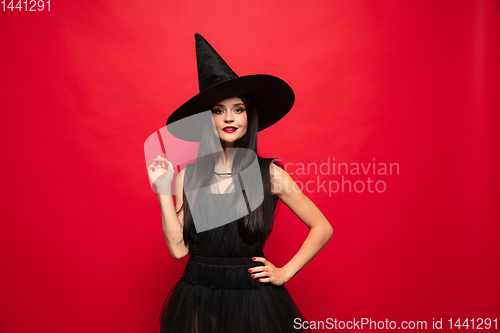 Image of Young woman in hat and dress as a witch on red background