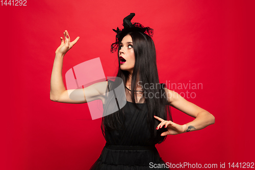 Image of Young woman in hat and dress as a witch on red background
