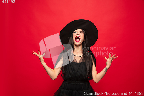 Image of Young woman in hat and dress as a witch on red background