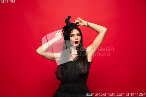 Image of Young woman in hat and dress as a witch on red background