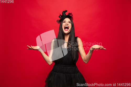 Image of Young woman in hat and dress as a witch on red background