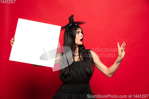 Image of Young woman in hat and dress as a witch on red background