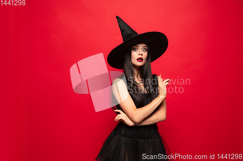 Image of Young woman in hat and dress as a witch on red background