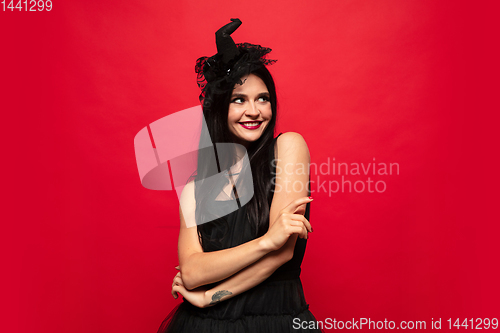 Image of Young woman in hat and dress as a witch on red background