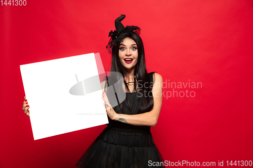 Image of Young woman in hat and dress as a witch on red background