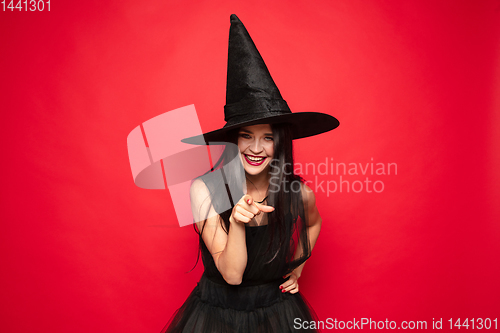Image of Young woman in hat and dress as a witch on red background
