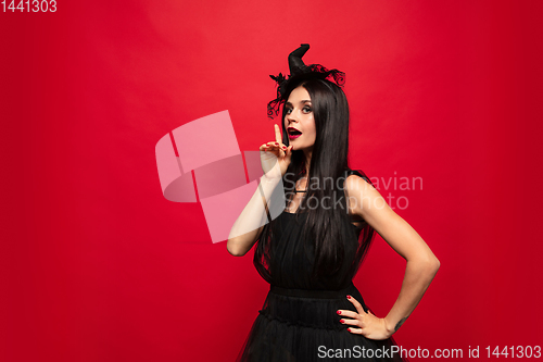 Image of Young woman in hat and dress as a witch on red background