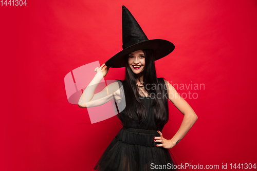 Image of Young woman in hat and dress as a witch on red background