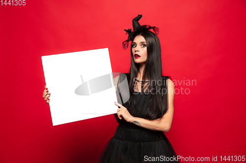 Image of Young woman in hat and dress as a witch on red background