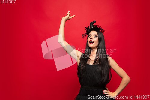 Image of Young woman in hat and dress as a witch on red background