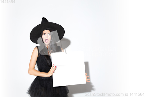 Image of Young woman in hat and dress as a witch on white background