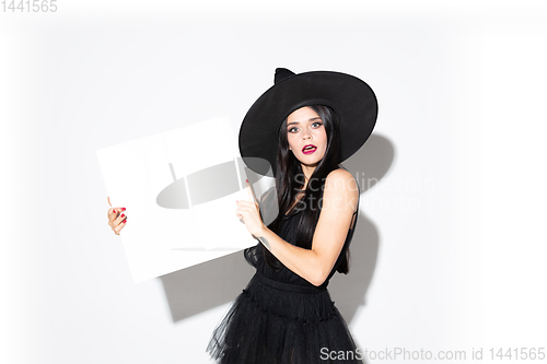 Image of Young woman in hat and dress as a witch on white background