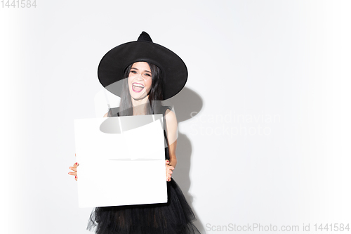 Image of Young woman in hat and dress as a witch on white background