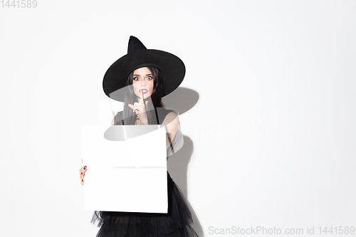 Image of Young woman in hat and dress as a witch on white background