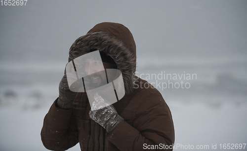 Image of man at winter in stormy weather wearing warm fur jacket