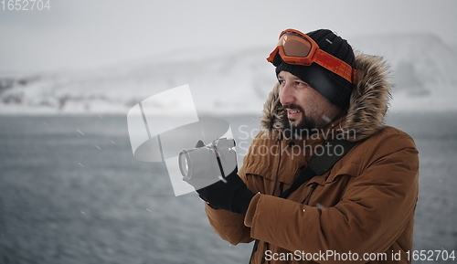 Image of photographer at winter in stormy weather wearing warm fur jacket