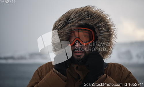 Image of man at winter in stormy weather wearing warm fur jacket