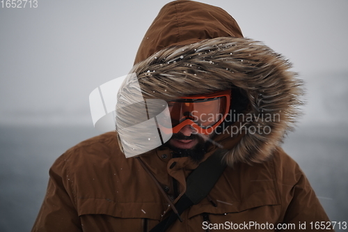 Image of man at winter in stormy weather wearing warm fur jacket