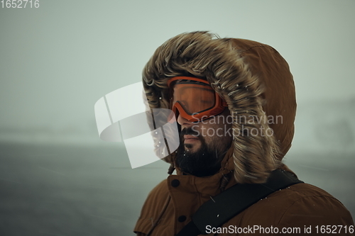 Image of man at winter in stormy weather wearing warm fur jacket